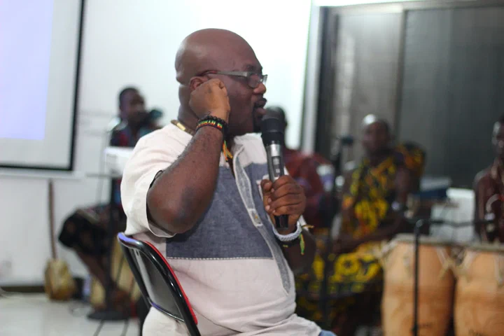 Foster Ofosu of Idea2Market makes a point into a microphone, drummers behind him