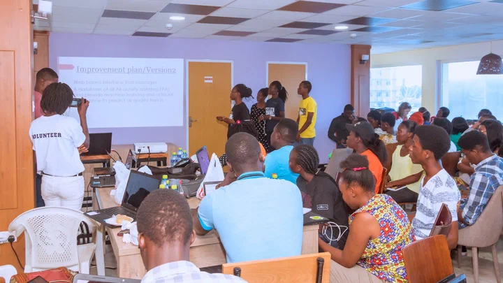 Datathon teams at their laptops while one team presents its improvement plan on a projected slide