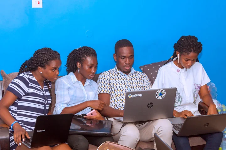 Four datathon participants work together on laptops on a sofa against a blue wall